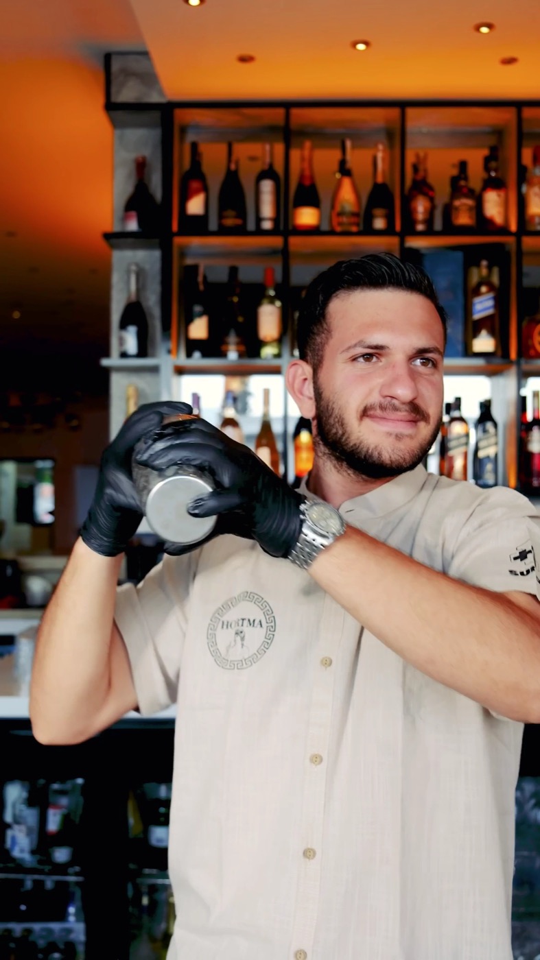 Hortma gömlekli barmen, dolu şişe rafları önünde kokteyl çalkalıyor