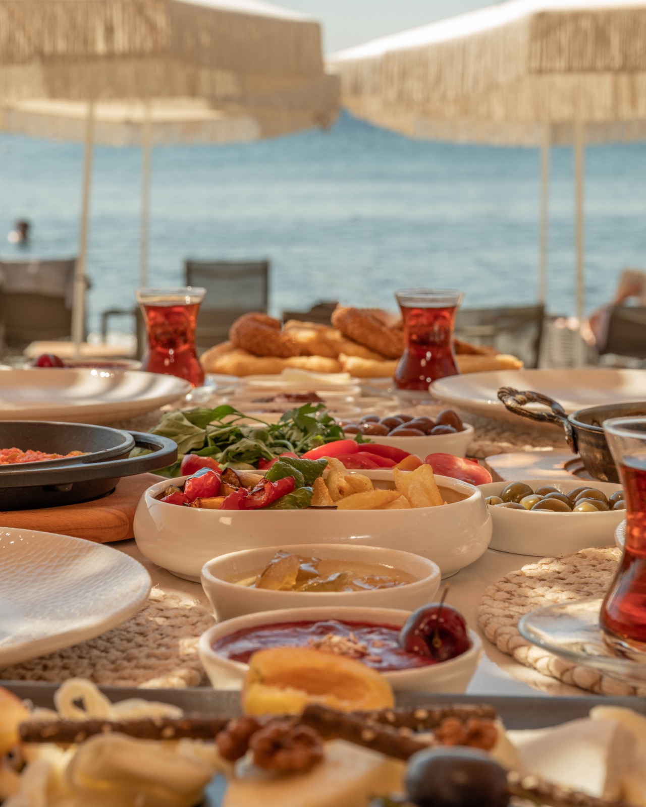 Denize karşı kurulmuş kahvaltı sofrası: çay, simit, salata, zeytin ve reçel