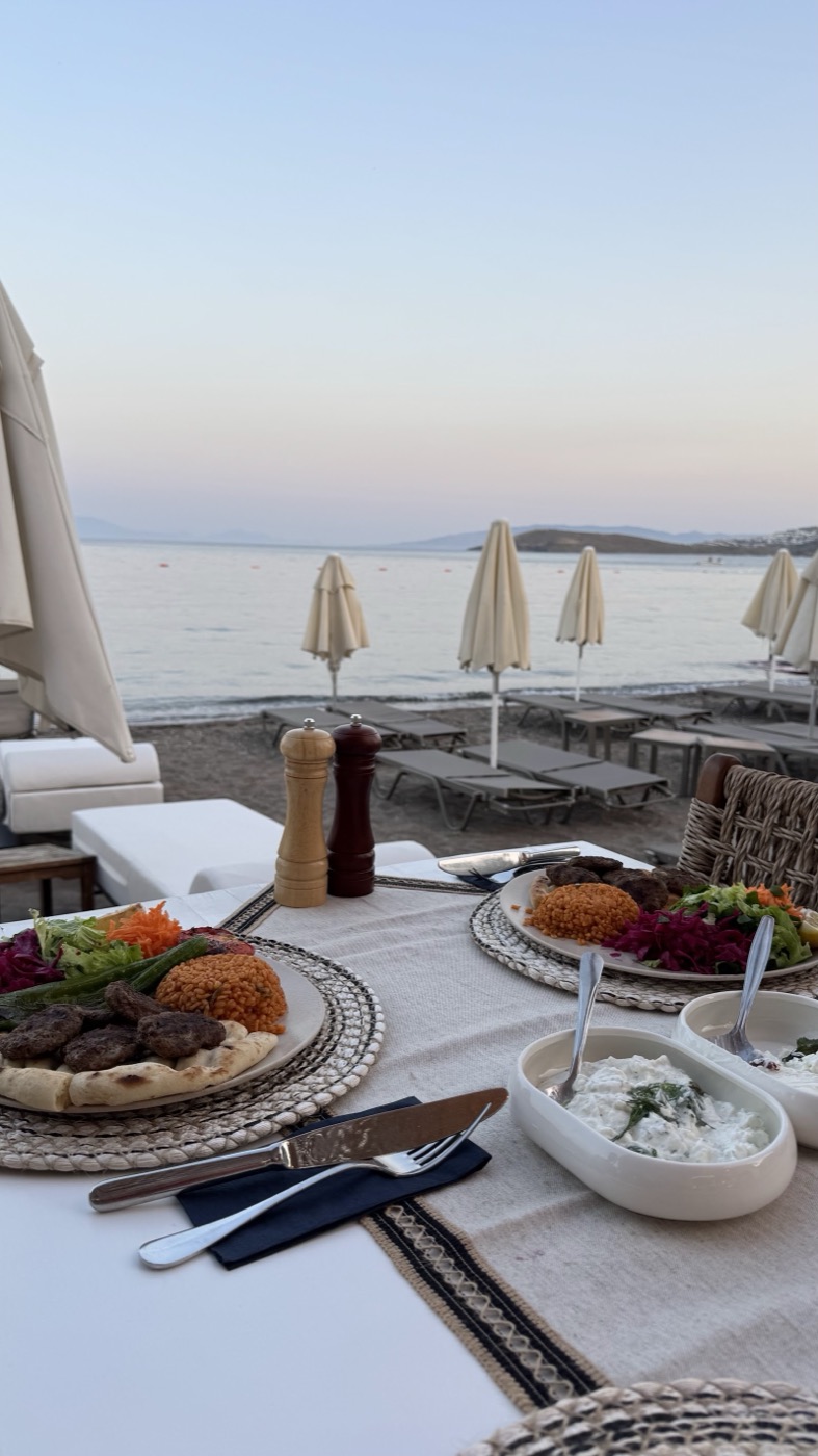 Pembe gün batımında denize karşı kebap, bulgur ve mezeli masa